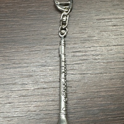 Porta-chaves prateado em forma de clarinete sobre madeira escura