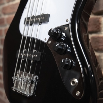 Baixo elétrico preto com escudo branco e botões pretos contra parede de tijolos.