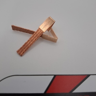 Pinça com ponta metálica dourada e corpo castanho sobre superfície branca com texto vermelho