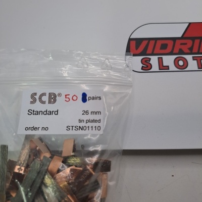 Peças metálicas pequenas em pacote plástico com etiqueta e logótipo parcial ao fundo.