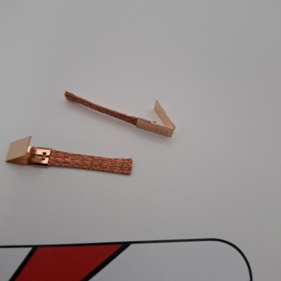 Dois cabos de cobre com extremidades dobradas sobre superfície branca com parte de logótipo visível.