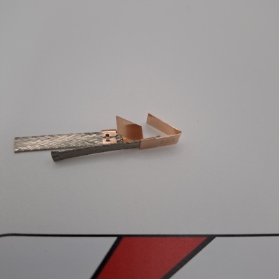 Peça metálica com textura e detalhes em cobre sobre fundo branco e gráfico vermelho e preto