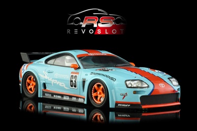 Modelo de carro de slot Toyota Supra azul claro com detalhes vermelhos, número 63, rodas laranja e logotipos de patrocinadores.