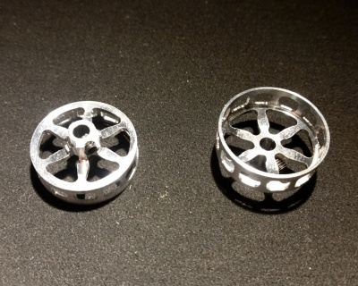 Dois pequenos objetos metálicos circulares prateados sobre superfície castanha.