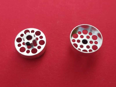 Dois objetos metálicos prateados com furos, em fundo vermelho