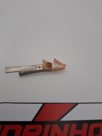 Peça metálica com textura e detalhes em cobre sobre fundo branco e gráfico vermelho e preto