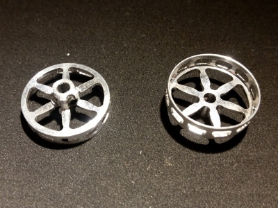 Duas peças metálicas circulares com formato de roda e raios sobre superfície escura