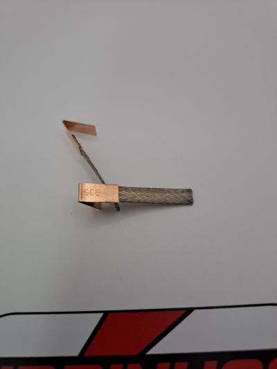 Peça metálica com lâminas de cobre e faixa cinzenta com inscrição SCB sobre fundo cinzento claro e logótipo vermelho e preto