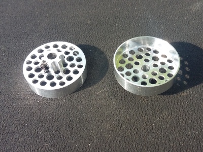 Dois objetos circulares metálicos prateados com vários orifícios sobre superfície preta