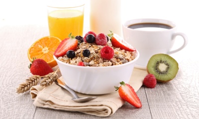Taça branca com muesli e frutos vermelhos, frutas frescas e bebidas numa mesa clara