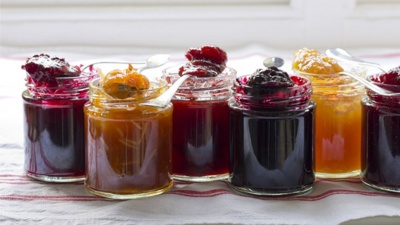 Seis frascos de compotas coloridas com colheres em cima de toalha riscada