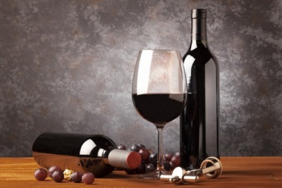 duas garrafas de vinho, um copo com vinho tinto, uvas e saca-rolhas sobre mesa de madeira