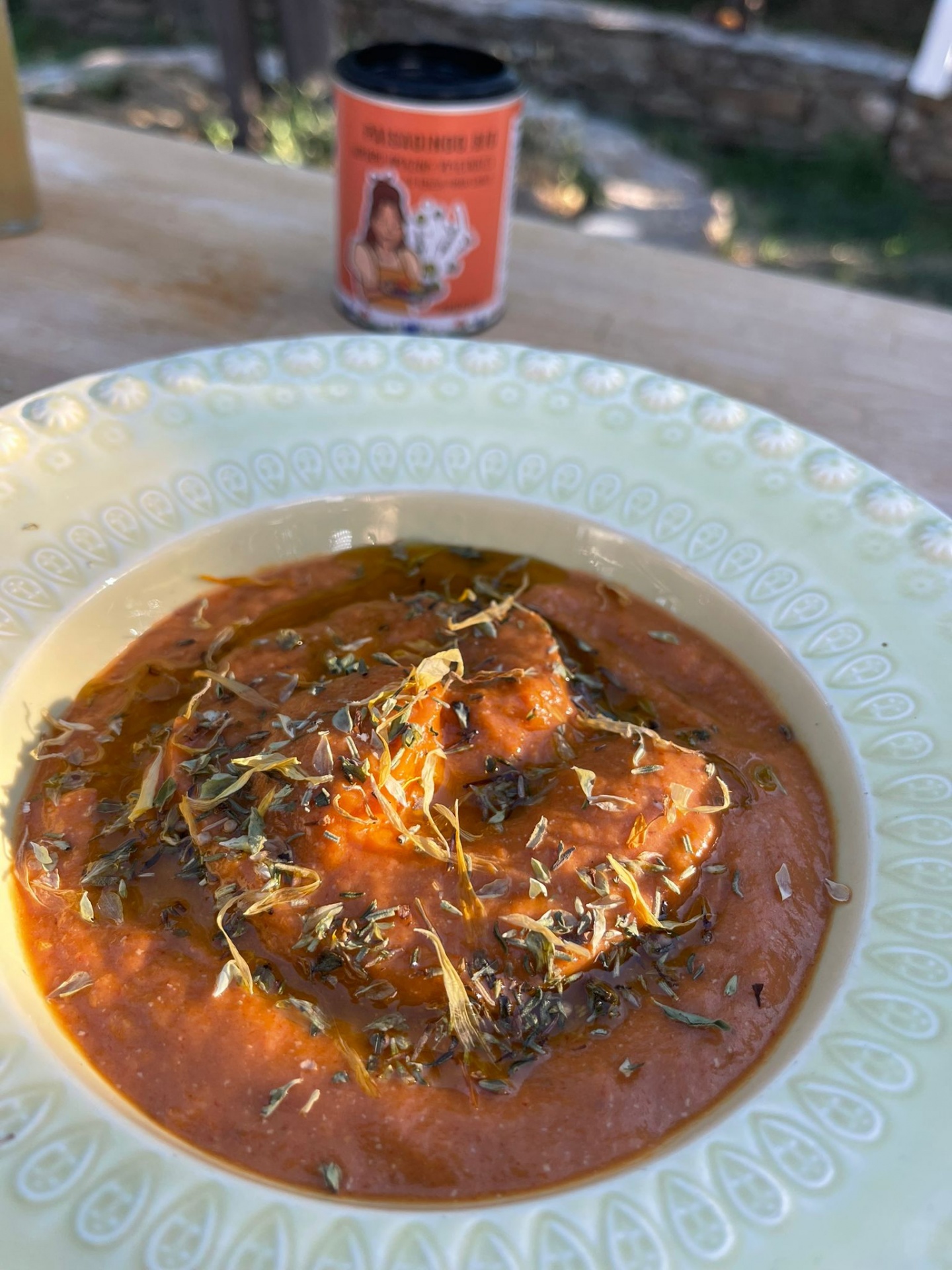 Prato de sopa vermelha com ervas secas e frasco de especiarias ao fundo