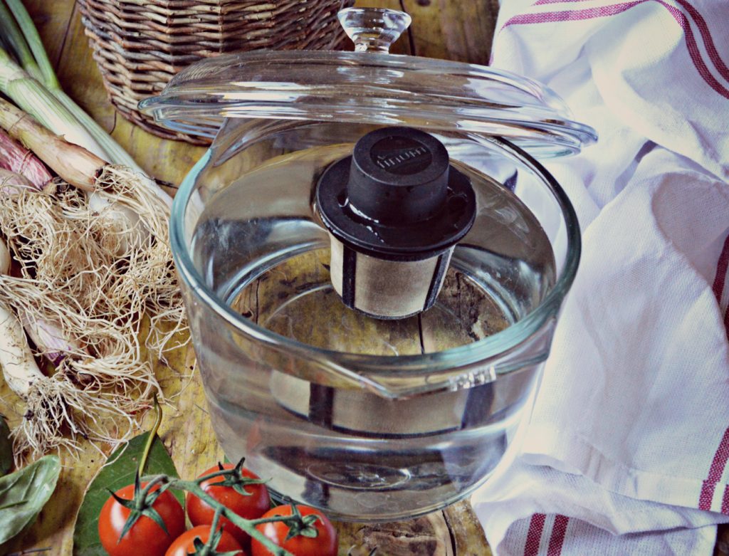Infusor flutuante com malha inox para chá/infusão - M FLOATING BASKET - Finum® Filtro de água dentro de jarro de vidro com tomates, cebolinhas e pano branco com riscas vermelhas.