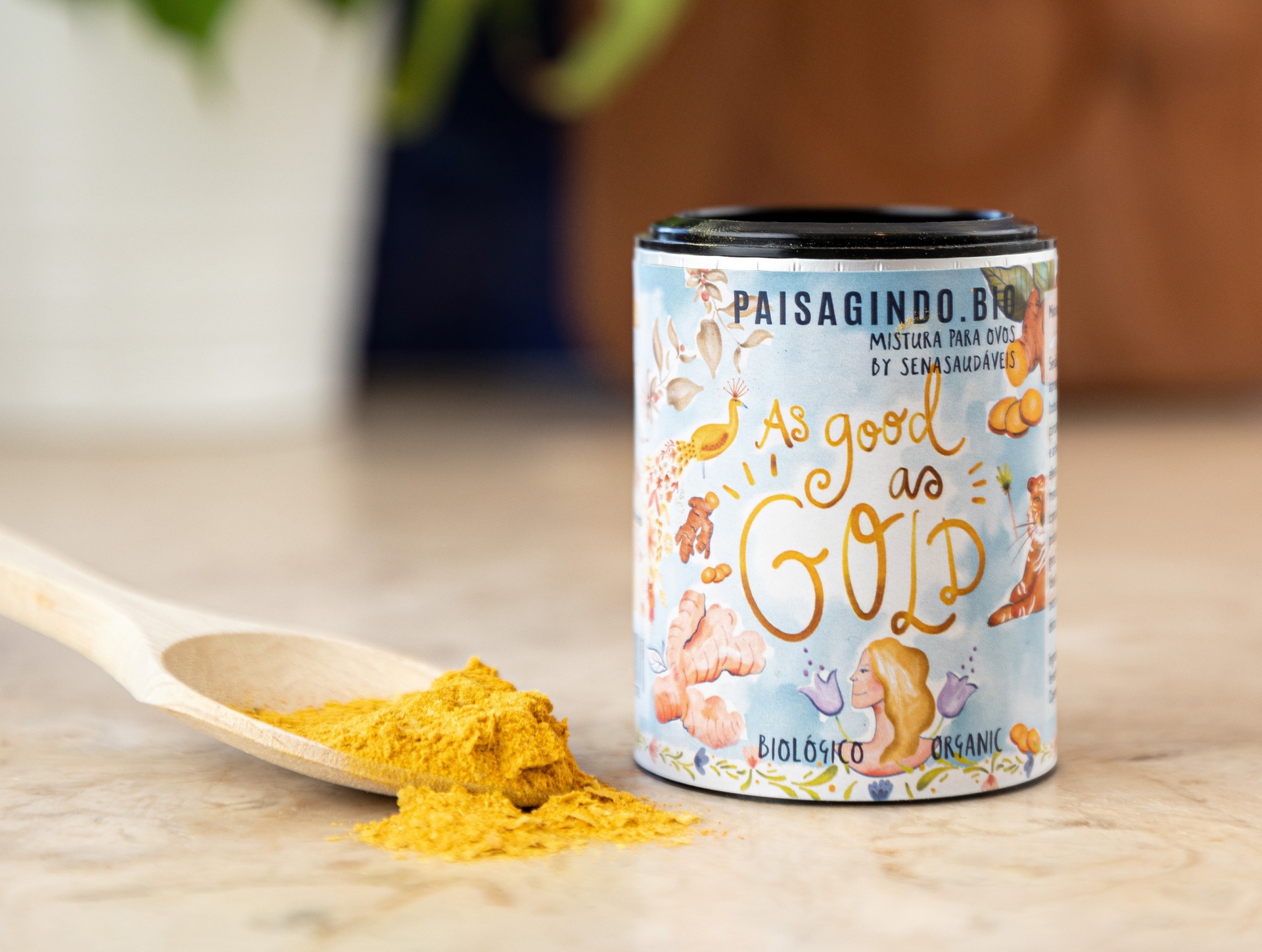 As Good as Gold by Senasaudáveis Frasco com pó amarelo e etiqueta ilustrada com cogumelos ao lado de colher de madeira