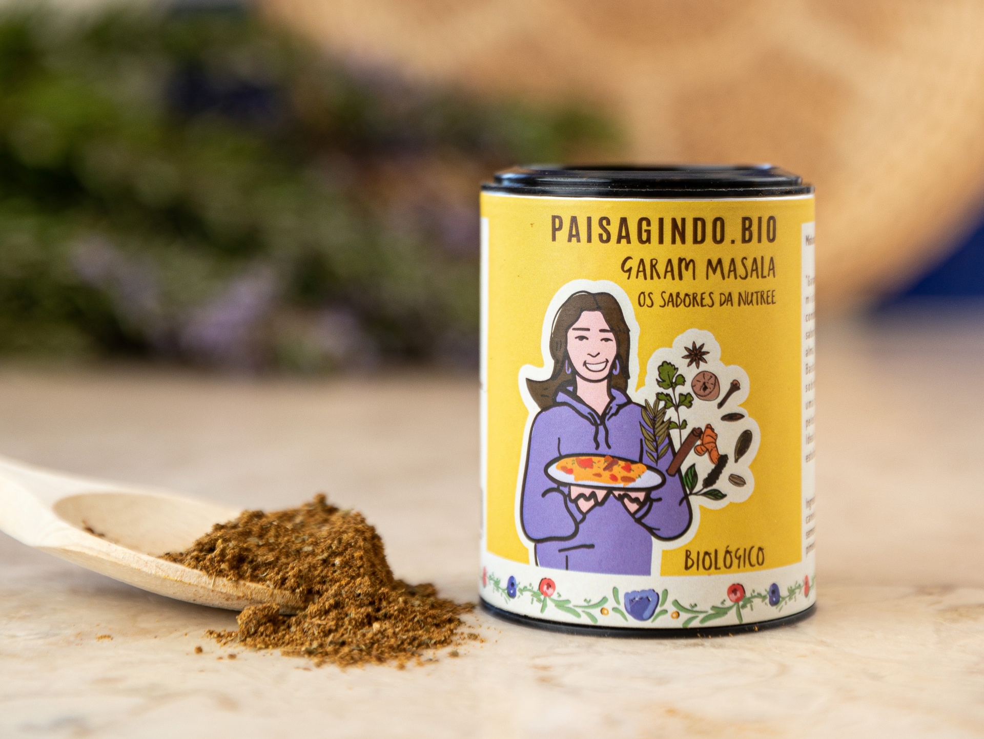 Garam Masala by Os Sabores da Nutree Frasco amarelo de garam masala com colher de madeira com especiaria em pó