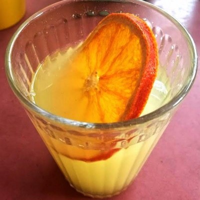 Copo transparente com bebida amarela e fatia de laranja seca