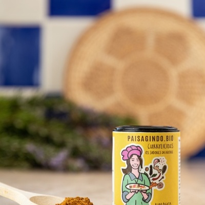 Recipiente amarelo com tempero em pó marrom e colher de madeira, fundo azulejos azuis e brancos