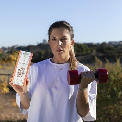 Mulher com camiseta branca segurando caixa de chá e haltere vermelho ao ar livre