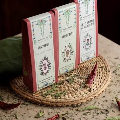 Três caixas de chá orgânico coloridas num suporte de palha com folhas e malaguetas à volta