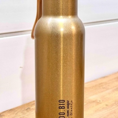 Garrafa metálica dourada com texto preto 'PAISAGINDO BIO' e alça de silicone laranja