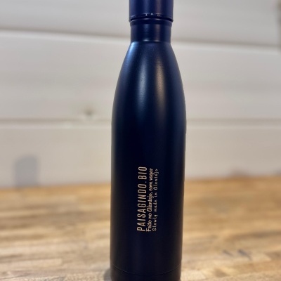 Garrafa térmica preta com texto dourado sobre mesa de madeira