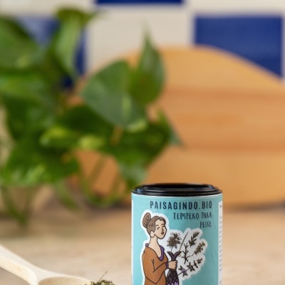 Embalagem pequena de tempero orgânico com ilustração e colher com ervas sobre bancada