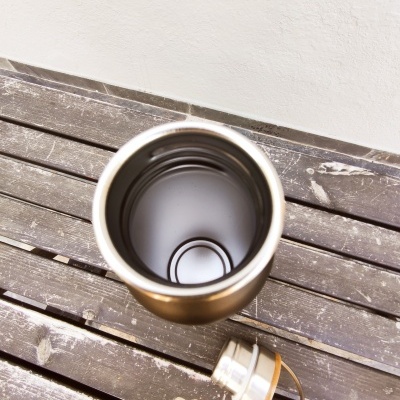 Frasco térmico dourado aberto sobre banco de madeira escura