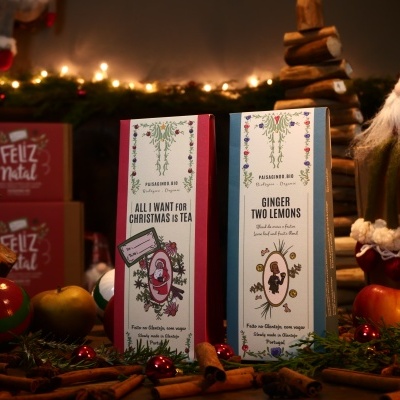 Dois pacotes de chá natalícios com padrões florais, rodeados por elementos de Natal como canelas e luzes