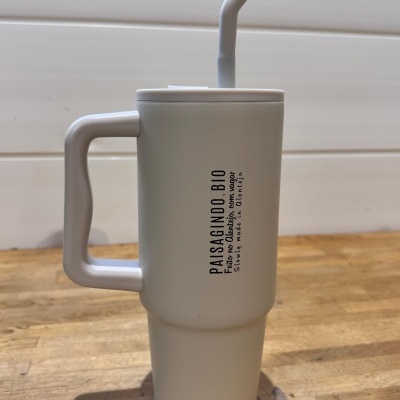 Copo térmico branco com canudo e pega sobre mesa de madeira