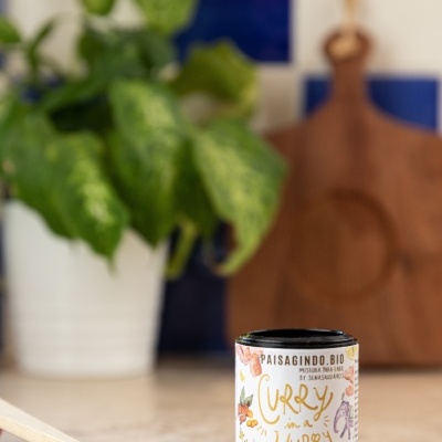 Latinha de curry em pó com rótulo ilustrado e colher de madeira com curry em pó