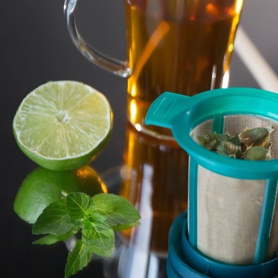 Filtro azul turquesa para chá com limão, folhas verdes e caneca de chá em vidro.