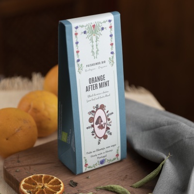 Embalagem azul clara de chá Orange After Mint com decoração floral junto a frutas e pano