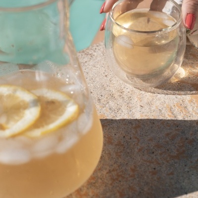 Jarro e chávena de vidro com bebida e limão numa superfície de pedra clara.