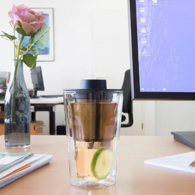 Copo de chá com rodela de pepino numa secretária de escritório com monitor e flor