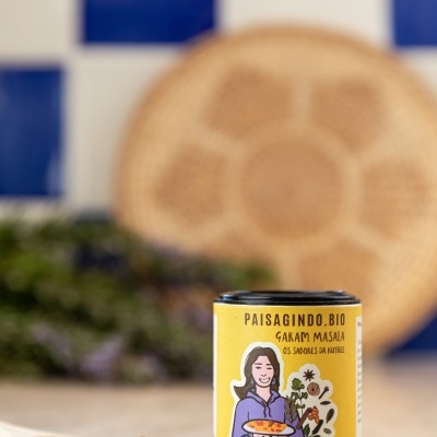 Frasco de especiarias Garam Masala biológico amarelo com colher de madeira e pó castanho sobre bancada com azulejos azuis no fundo