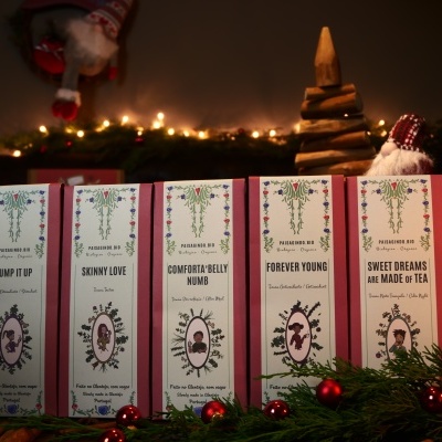 Cinco caixas de chá com nomes diferentes etiquetados, em ambiente com decoração de Natal.