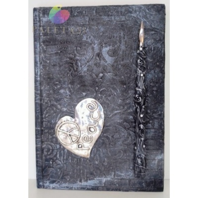 Caderno preto com coração metálico e caneta decorativa ao lado