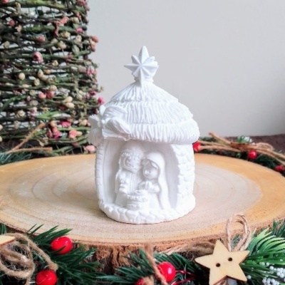 Figura de presépio branca em cerâmica com casal dentro de uma gruta e decoração natalícia ao redor