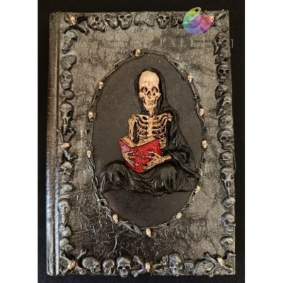 Capa preta com moldura de caveiras e esqueleto a ler um livro vermelho