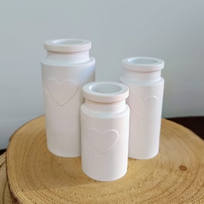 Três frascos brancos de cerâmica com coração em relevo sobre madeira redonda