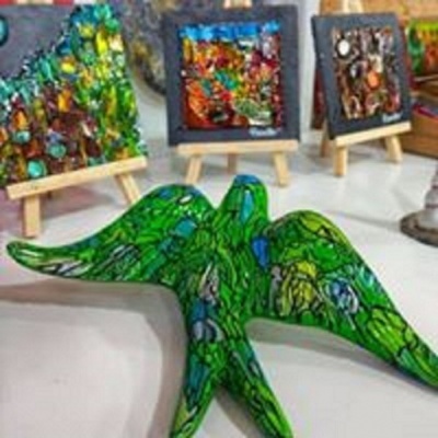 Escultura de pássaro verde com quadros coloridos em mini cavaletes ao fundo