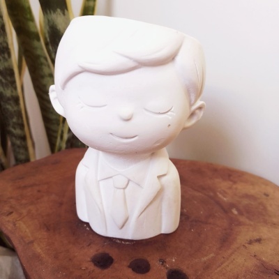 Escultura decorativa branca em forma de boneco com roupa formal sobre madeira rústica