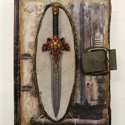 Caderno rígido com capa decorada com imagem de punhal e fecho de fivela metálica