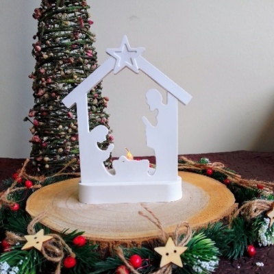 Miniatura decorativa de presépio branco sobre base de madeira com vela e decoração natalícia