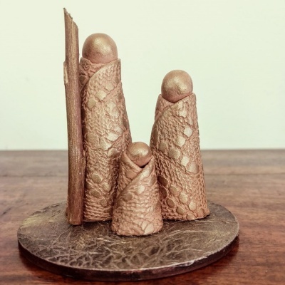 Escultura decorativa de três figuras em tecido texturizado castanho com esferas, sobre base de couro escuro