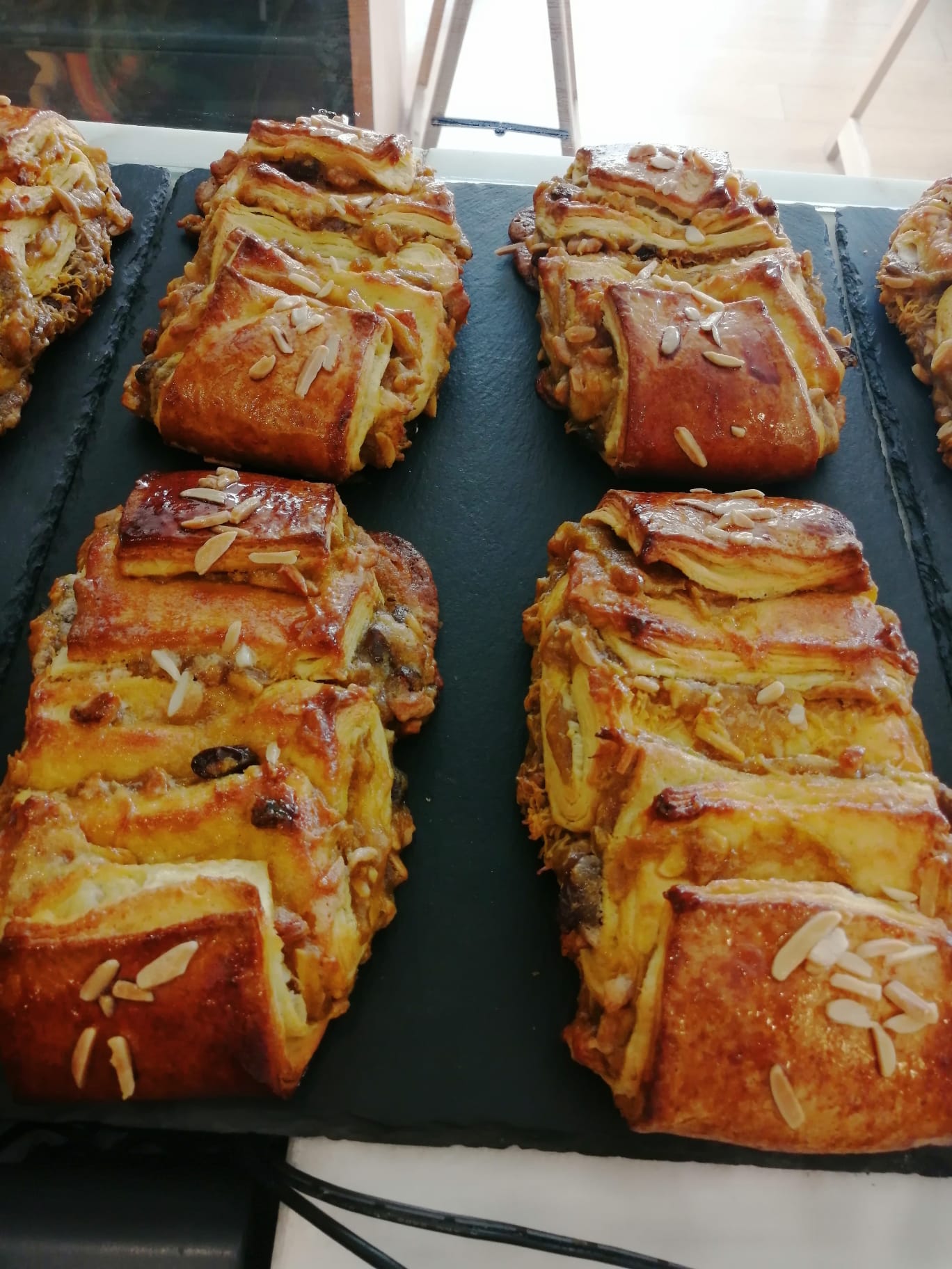 Folhados com amêndoas laminadas sobre superfície preta numa pastelaria.