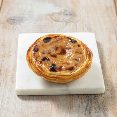 Pastel de nata sobre placa de mármore branco em mesa de madeira clara