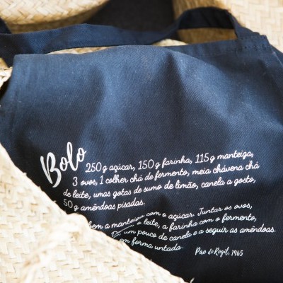 Saco de tecido azul com texto branco sobre receita, dentro de chapéus de palha