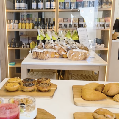 Produtos variados incluindo vinhos, bolachas, pastéis de nata e bebida sobre mesa branca e prateleiras de madeira